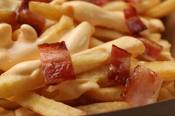 Tasty potato fries, cheese sauce and bacon in paper container, closeup