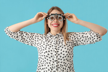 Young woman in trial frame checking her eyesight on blue background