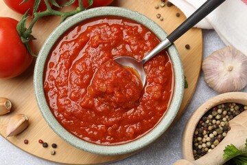 Homemade tomato sauce in bowl, spoon and fresh ingredients on light grey table, flat lay