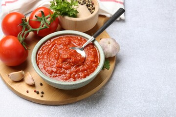 Homemade tomato sauce in bowl, spoon and fresh ingredients on light grey table. Space for text