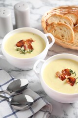 Tasty potato soup with bacon and rosemary in bowls served on white marble table
