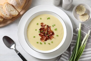 Tasty potato soup with bacon in bowl served on white wooden table, flat lay