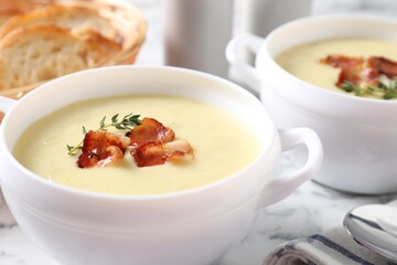 Tasty potato soup with bacon and rosemary in bowls on white table, closeup