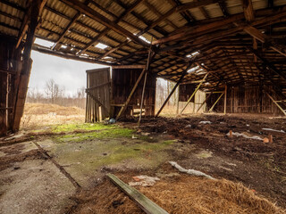 Fototapeta na wymiar Wooden barn in abandoned farm with rubbish inside, holes in roof and open doors. Economy in agriculture industry, cost of running business. Effect of recession on farming.