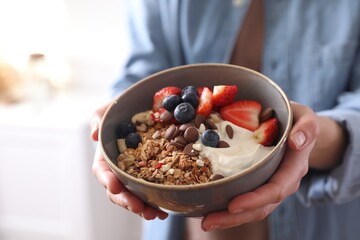 Woman holding bowl of tasty granola on blurred background, closeup