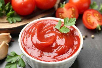 Delicious tomato ketchup in bowl, parsley and garlic on grey table, closeup