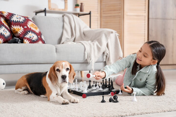 Cute little Asian girl with Beagle dog playing chess at home