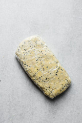 Overhead view of raw black sesame scones dough being in plastic wrap on a marble counter top,...