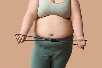 Young overweight woman with fitness expander on brown background, closeup. Weight loss concept