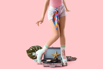 Young woman in roller skates with record player on pink background
