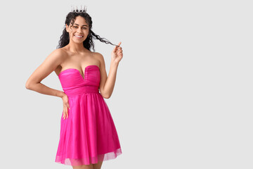 Happy young African-American woman in stylish pink prom dress and tiara on grey background