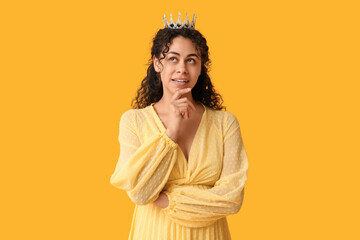 Thoughtful young African-American woman in stylish prom dress and tiara on yellow background