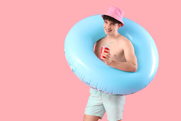 Handsome young happy man with inflatable ring and cup of cold soda on pink background