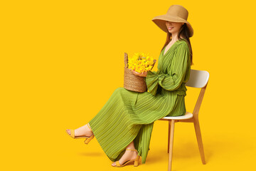 Beautiful young happy woman with bag of beautiful narcissus flowers sitting on chair against yellow...