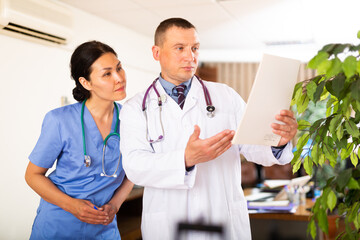 Experienced male doctor advising his female colleague about diagnosis of patient while reviewing...