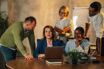 Interracial staff working on laptop and brainstorming ideas at office.