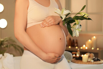 Young pregnant woman with flowers in dark spa salon, closeup