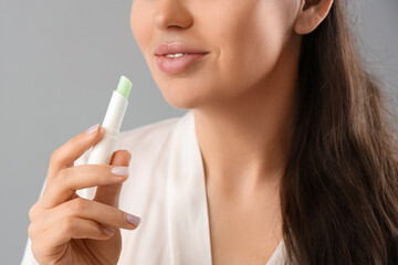 Obraz premium Young woman with lip balm on grey background, closeup