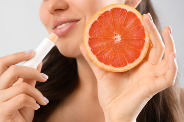 Young woman with lip balm and grapefruit on light background, closeup
