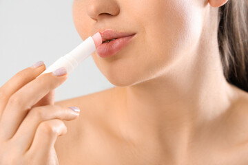 Young woman applying lip balm on light background, closeup