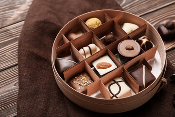 Box with delicious chocolate candies and fabric napkin on wooden background