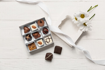 Box with tasty candies and chamomiles on wooden background