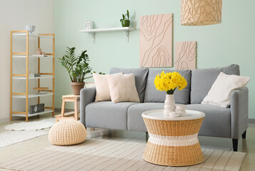 Beautiful interior of living room with grey sofa, coffee table and vase of narcissus flowers