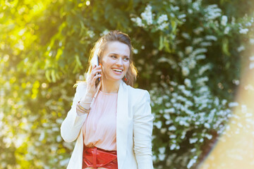 happy woman in dress and jacket in city using smartphone