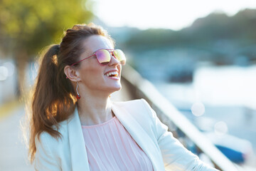smiling trendy woman in pink dress and white jacket in city