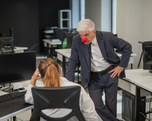 Elderly Caucasian man wearing a clown nose swears at his subordinate in the office. 