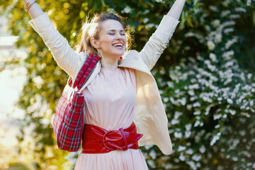 happy trendy woman in pink dress and white jacket in city