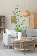Interior of beautiful living room with cozy sofa, coffee table and blooming tree branches in vase