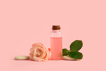 Bottle of cosmetic oil, rose and spa stones on pink background