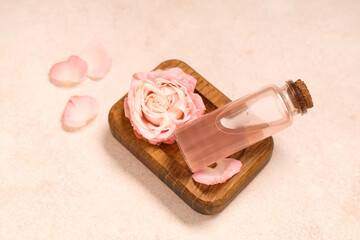 Composition with bottle of cosmetic oil, wooden tray, petals and rose on pink background