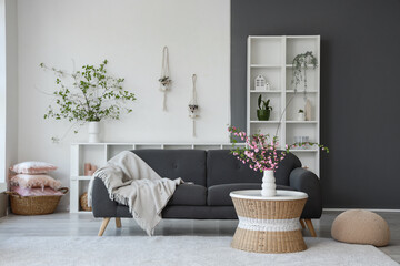 Stylish interior of living room with sofa and coffee table with blooming branches