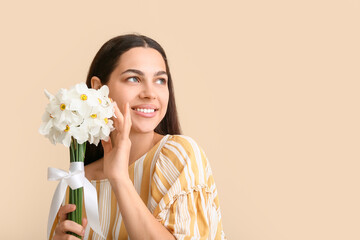 Beautiful young woman with bouquet of white daffodil flowers on beige background