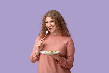 Happy young woman with fork and plate of tasty ravioli on lilac background