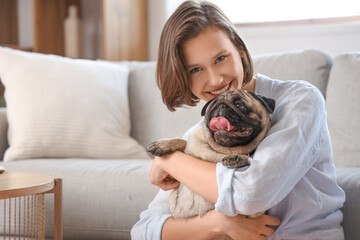 Young woman with cute pug dog sitting on floor in living room, closeup