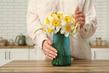 Naklejka premium Young woman touching vase with yellow flowers on table in stylish kitchen