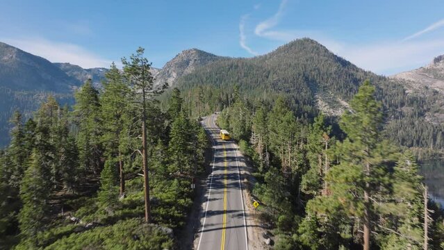 Experience an aerial perspective of a winding mountain road in Lake Tahoe, California, as a yellow school bus navigates the scenic route below. Shot in stunning 4K footage.
