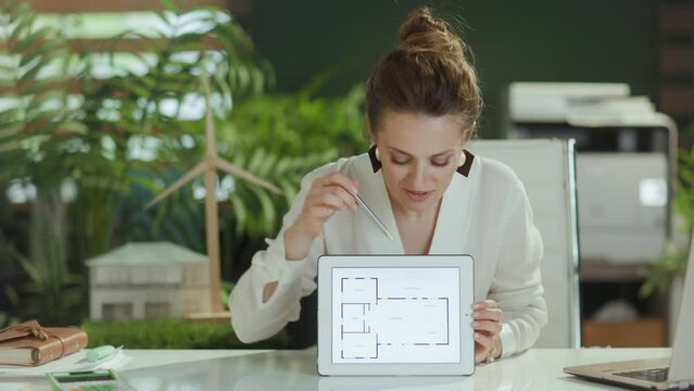 Sustainable real estate business. happy modern middle aged woman real estate agent in modern green office in white blouse using digital tablet.