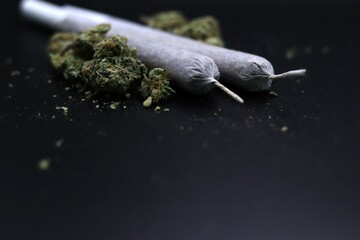 two rolled joints placed alongside scattered marijuana buds on a dark surface. concepts: medical...