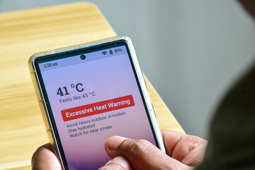 Man using his mobile phone displaying alertness for excessive heat warning. Severe weather El Nino...