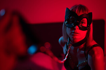 Blonde girl in a leather mask and handcuffs in the bedroom in red blue neon light. Role-playing...