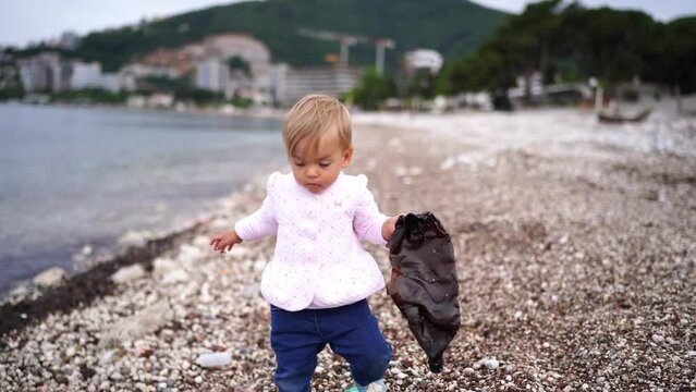 Little girl carries a crumpled plastic bottle on the beach. High quality 4k footage