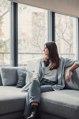 Portrait of happy dreamy young woman looking away, standing with folded arms in modern living room, visualizing future, recollecting good memories, planning weekend or thinking of problem solutions..