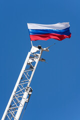 The official national tricolor flag of Russia mounted on top of a raised fire escape against a blue...