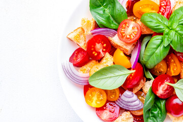 Italian salad with tomatoes, stale bread, red onion, olive oil, salt and green basil, white table background, top view close up