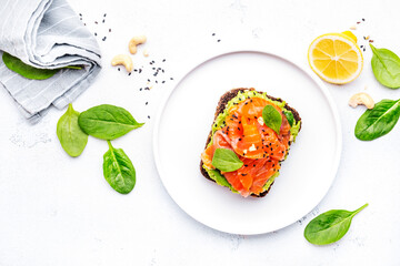 Avocado and salmon toast on rye bread with spinach, cashew and sesame seeds, white table...
