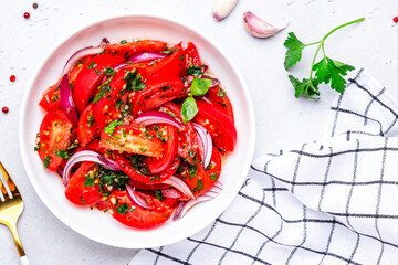 Fresh juicy summer tomato salad with parsley garlic and olive oil dressing and red onion, white table background, top view